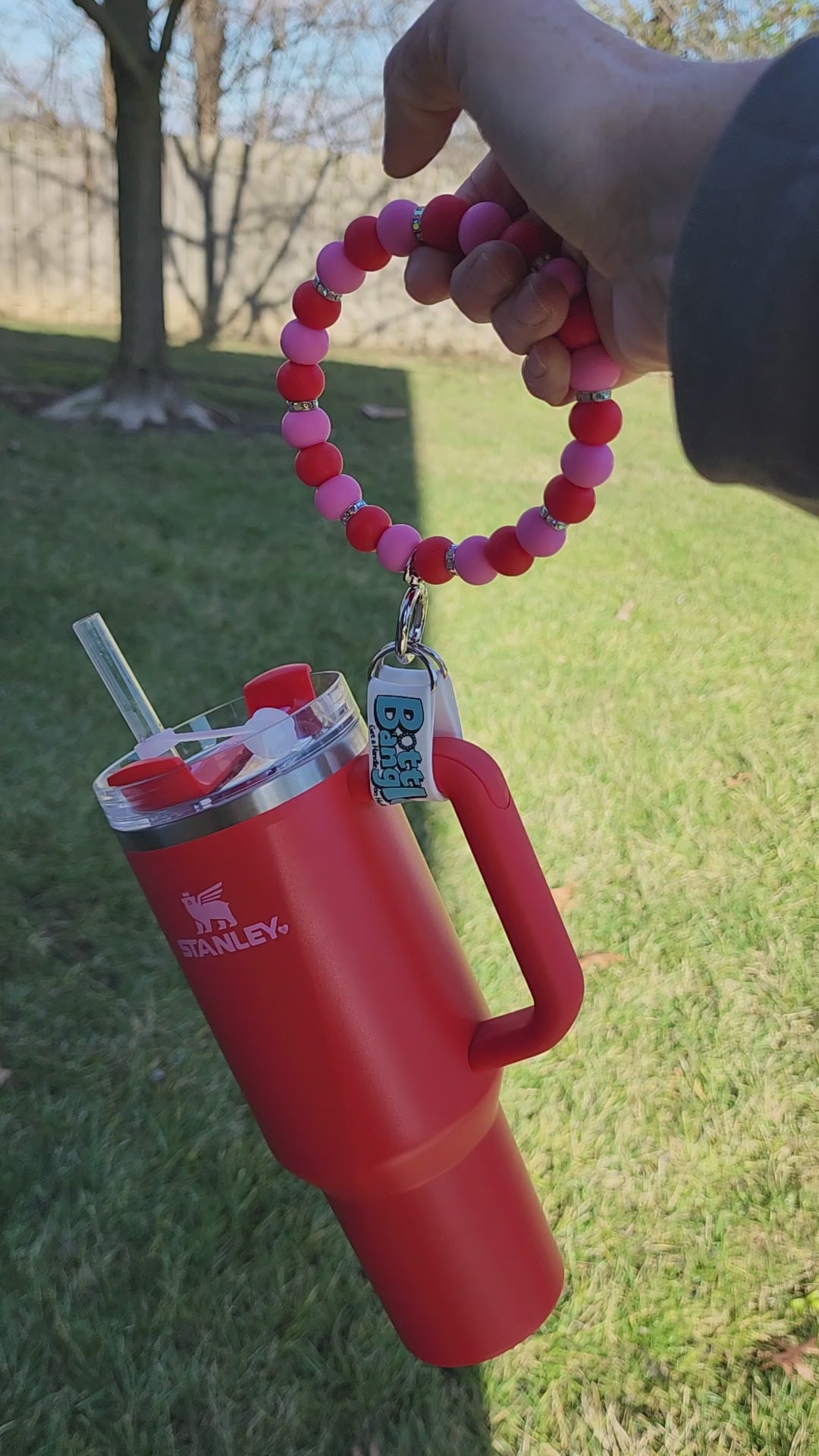 Load video: Red 40 oz Tumbler full of water and ice with a Red and Pink Bottle Bangle attached to the handle. Bottle Bangle is being bouced and shaken vigorously to demonstrate the weight bearing ability of the Bottle Bangle.